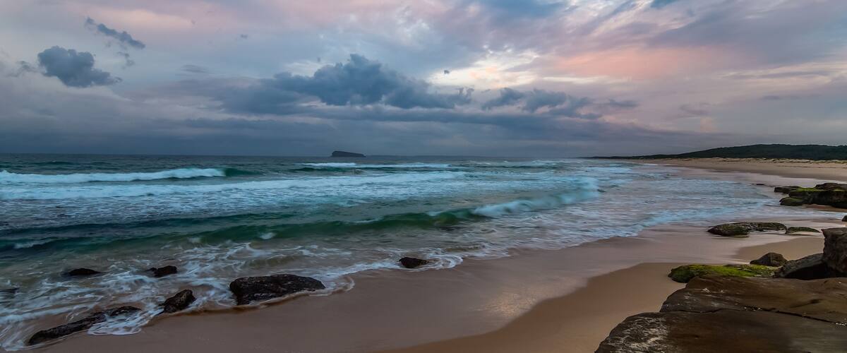 A beach with waves, rocks, and a cloudy sky.