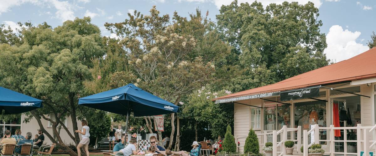 An outdoor cafe with tables and chairs, blue umbrellas, and a building with a sign reading "McCormick & Creed".
