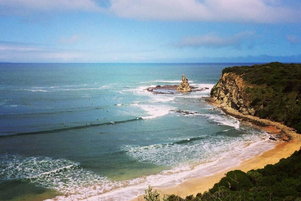 Un paysage côtier avec une plage de sable, des vagues de l’océan et un promontoire rocheux.