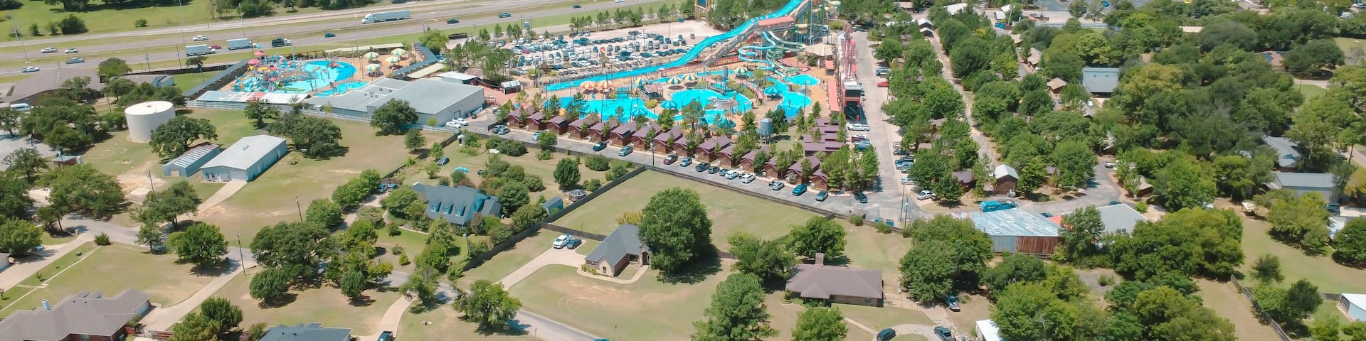 An aerial view of a theme park with a water slide, parking lots, and surrounding residential areas.