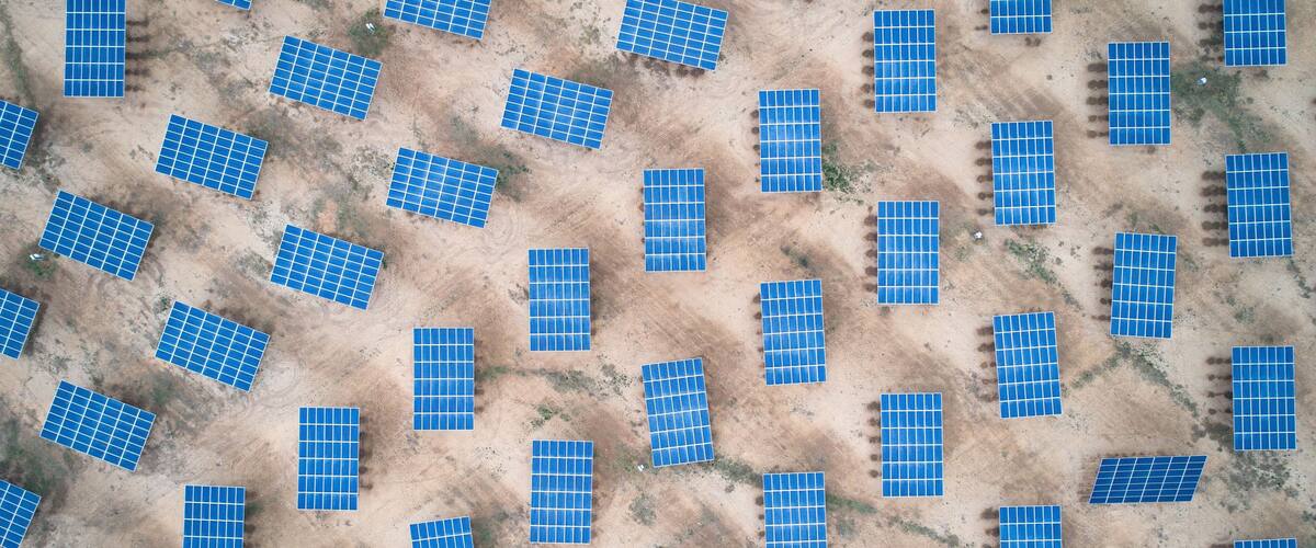 An aerial view of solar panels arranged in a grid pattern on a dry, barren landscape.