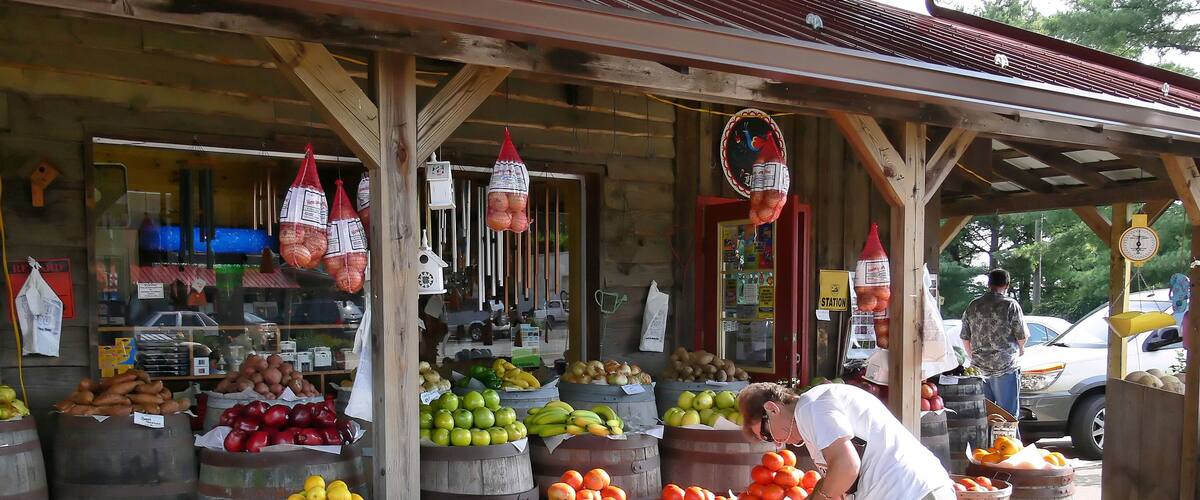A fruit stand with wooden barrels and a man picking oranges.