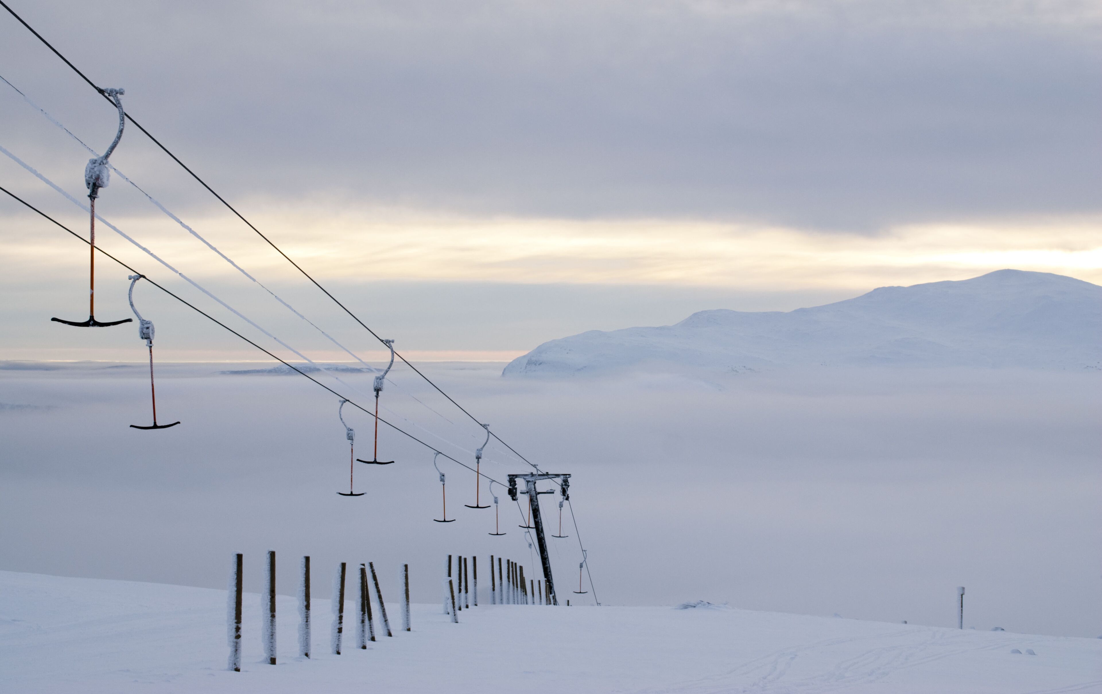 A snow-covered ski lift with cables extending over a snowy landscape and mountains in the background.