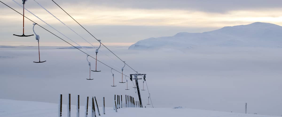 A snow-covered ski lift with cables extending over a snowy landscape and mountains in the background.