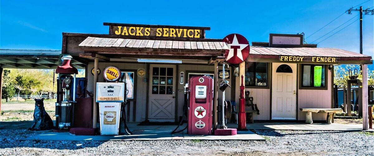 A vintage gas station named 'JACKS SERVICE' with a Shell sign, a Texaco sign, and a Freddy Fender sign.