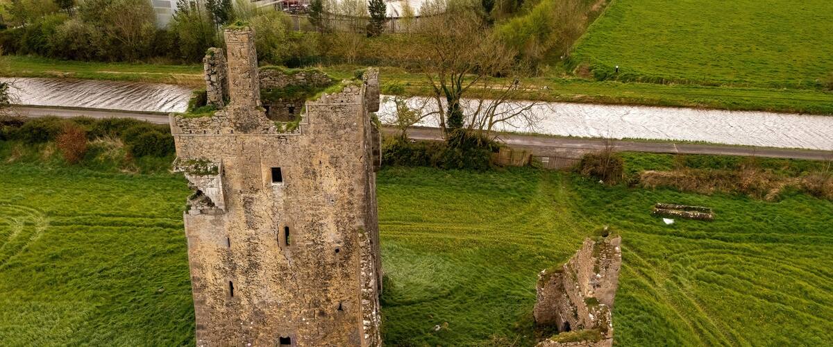 An aerial view of a medieval stone tower surrounded by lush green fields and a river.
