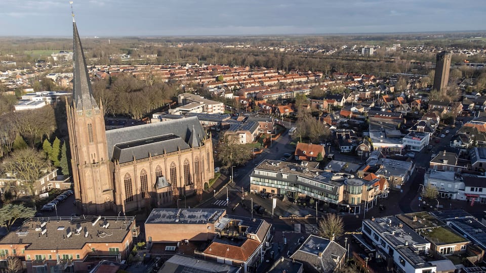An aerial view of a town with a prominent church featuring a tall spire and a large clock tower.
