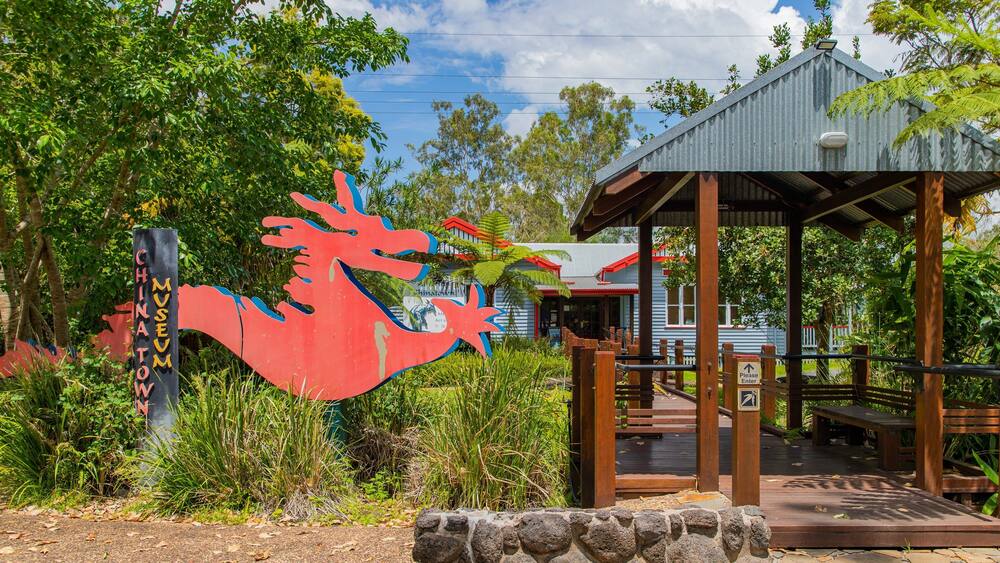 Une sculpture rouge représentant un poisson, un pavillon en bois et un bâtiment avec un toit rouge.