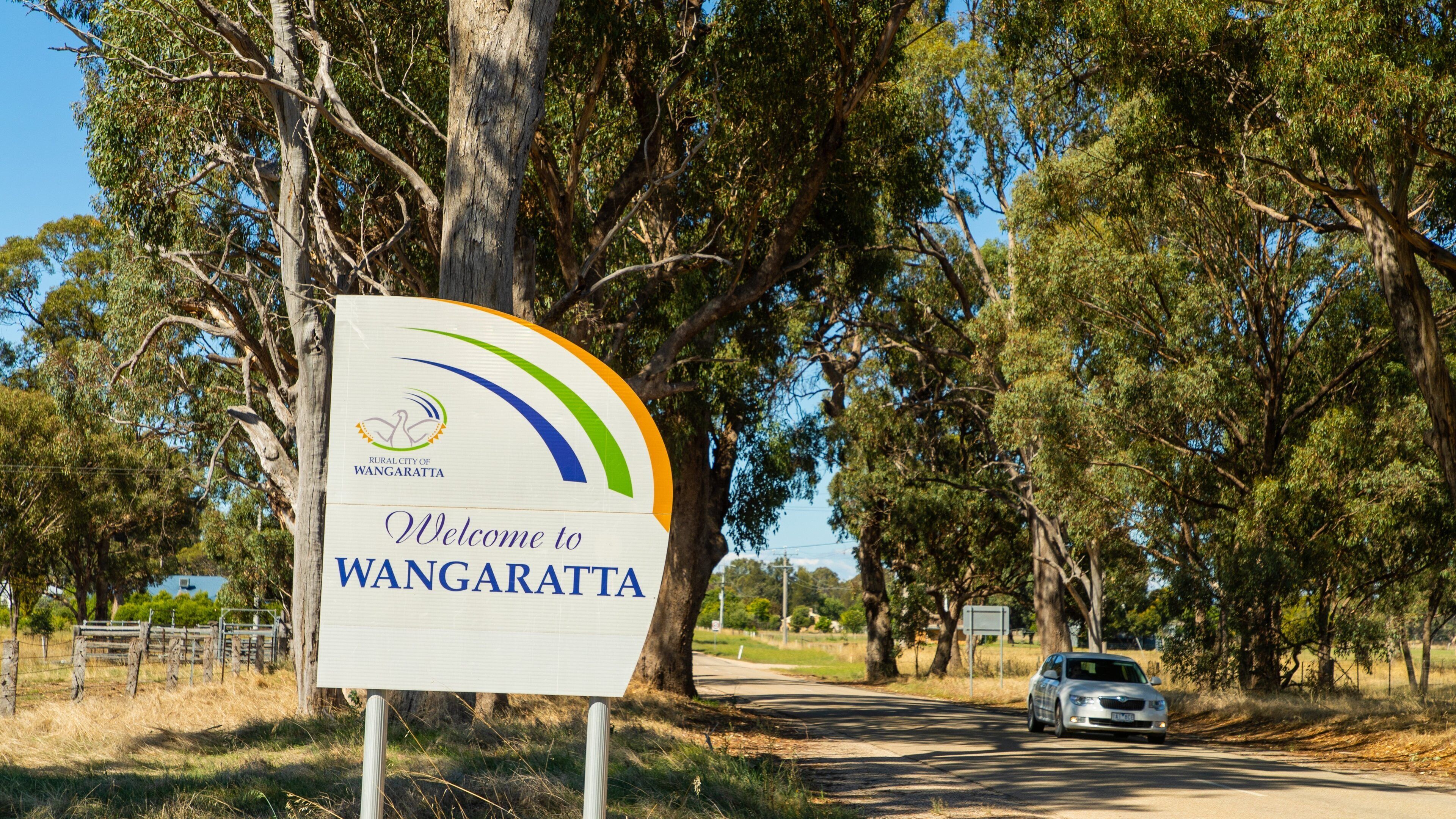 A welcome sign for Wangaratta with a car parked on the roadside.