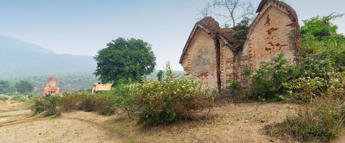 An ancient, weathered temple with two large, curved structures surrounded by overgrown vegetation.