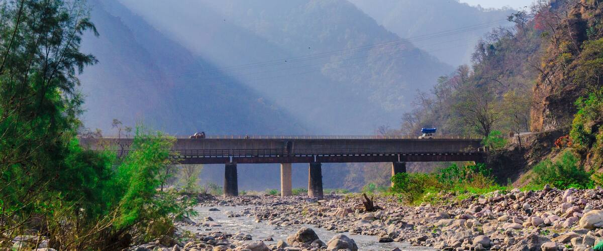 A bridge over a rocky river with mountains in the background.
