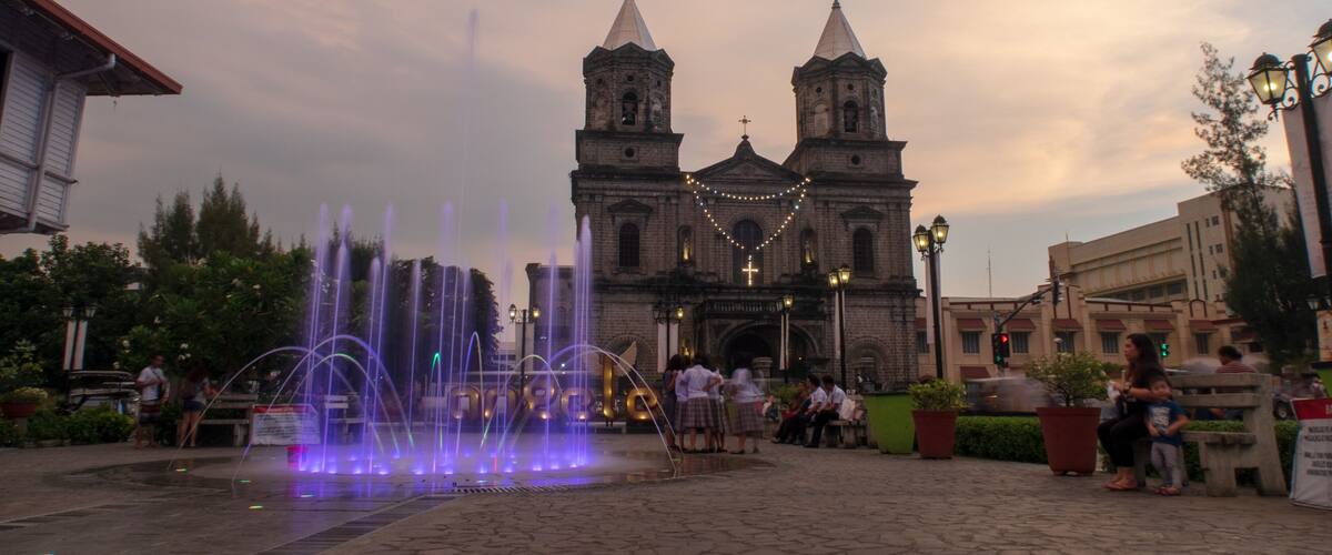 A historic church with twin towers, a fountain with water jets, and people in the foreground.