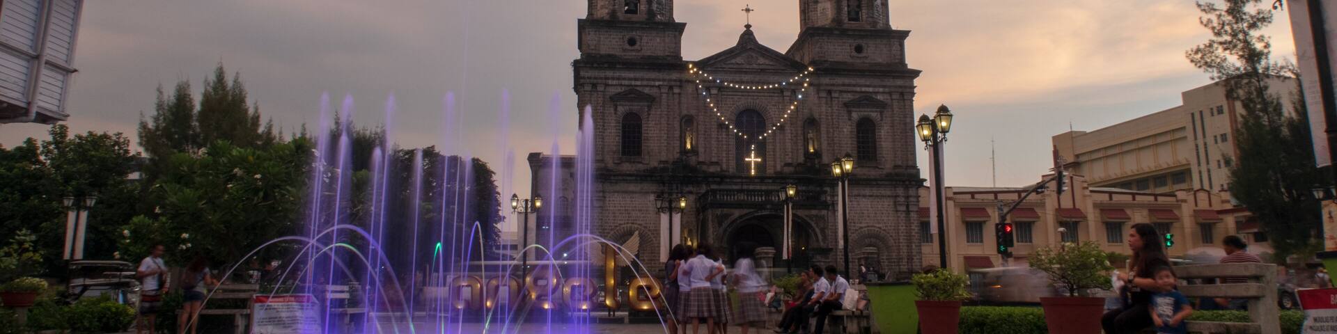 A historic church with twin towers, a fountain with water jets, and people in the foreground.