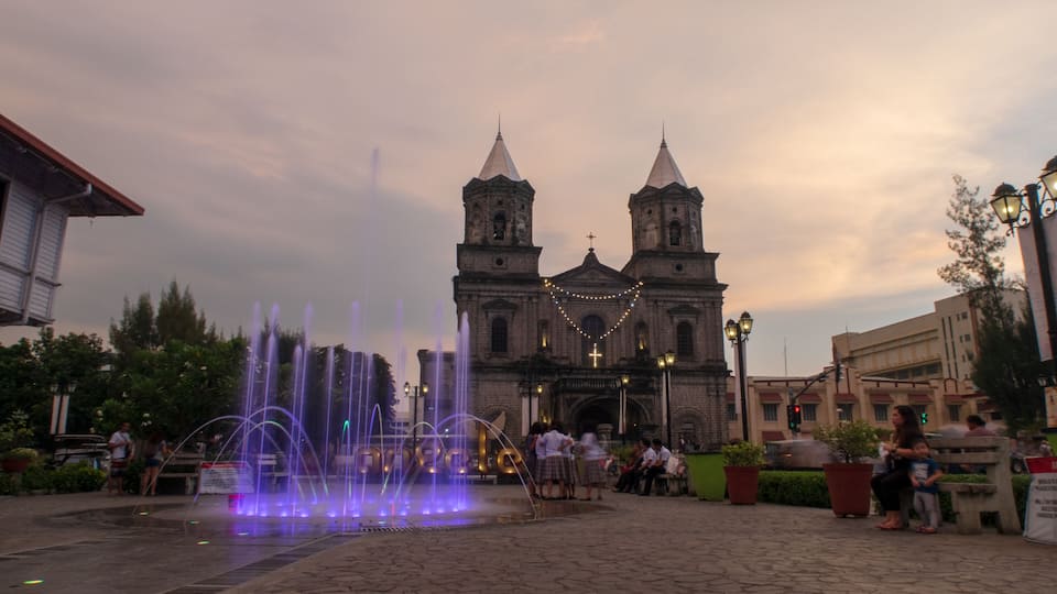 A historic church with twin towers, a fountain with water jets, and people in the foreground.
