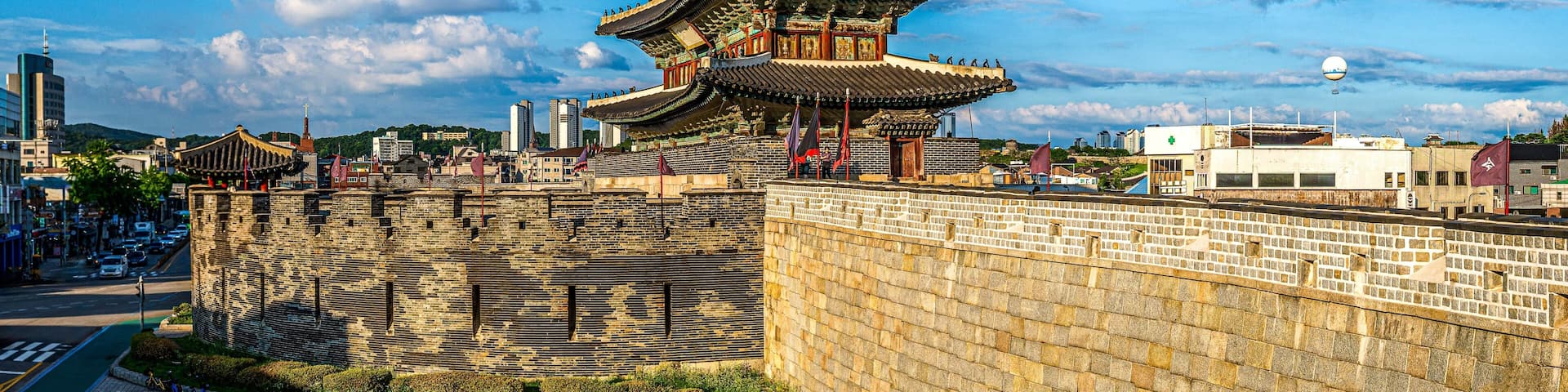 A traditional Korean palace with a multi-tiered roof, surrounded by a stone wall and set against a clear blue sky.