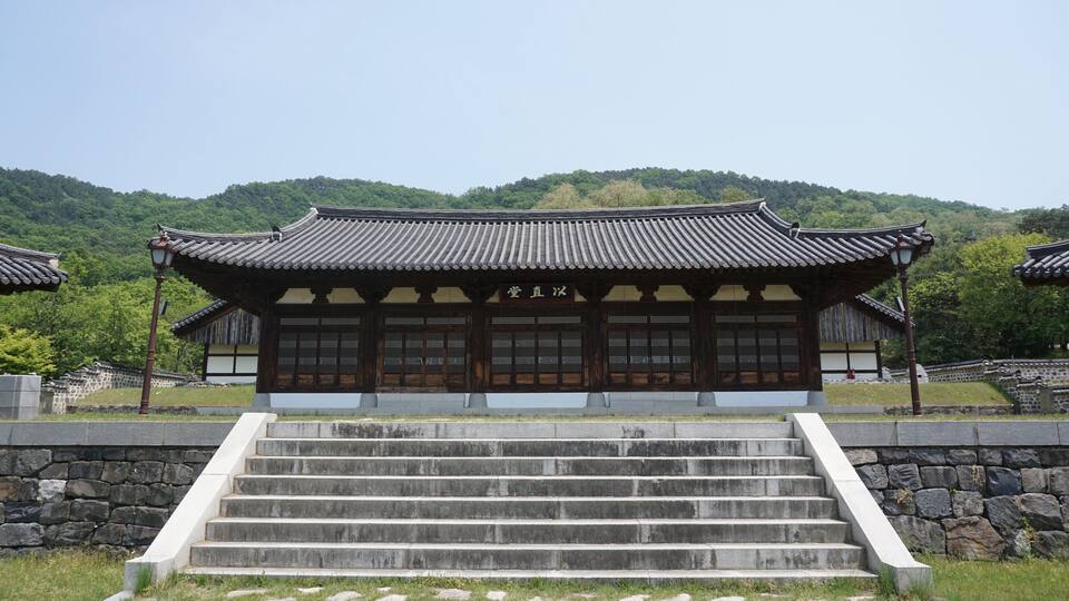 A traditional Korean building with a tiled roof and wooden doors, surrounded by stone steps and a stone wall.