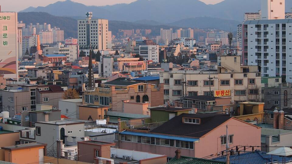 A densely packed urban area with various buildings, including residential and commercial structures, and mountains in the background.