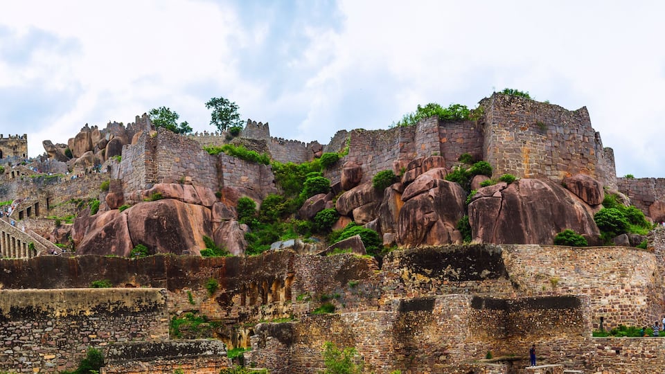A historic stone fortress with battlements, perched on a rocky outcrop with lush greenery.