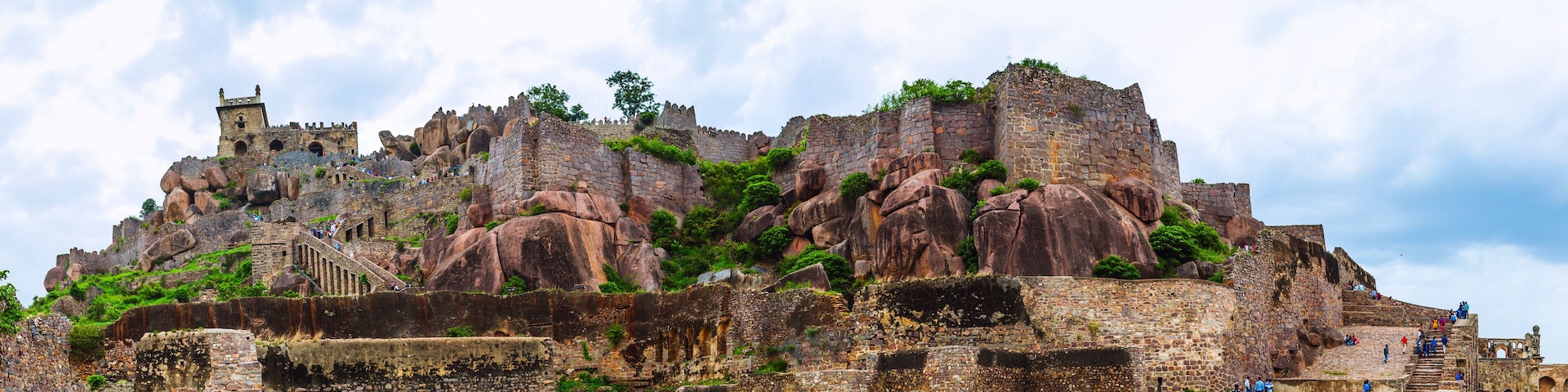 Eine historische Steinburg mit Zinnen thront auf einem felsigen Vorsprung inmitten üppiger Vegetation.