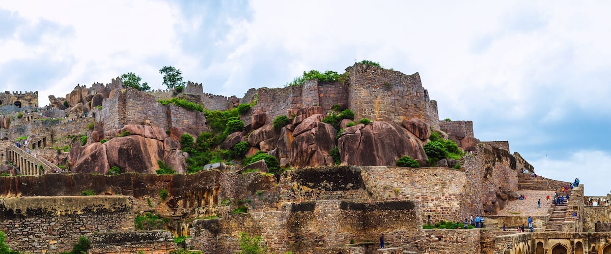 A historic stone fortress with battlements, perched on a rocky outcrop with lush greenery.
