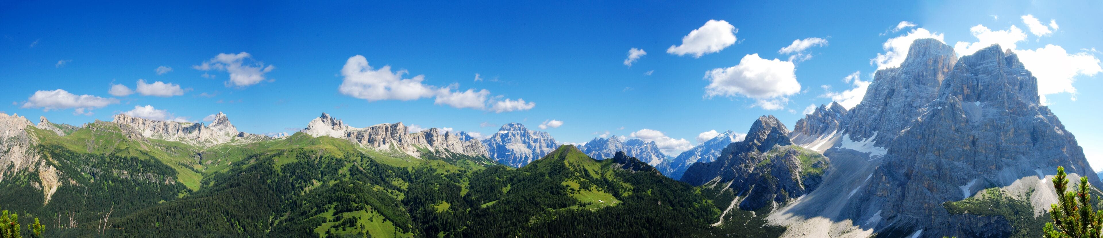 A mountain range with prominent peaks, lush green valleys, and a clear blue sky.