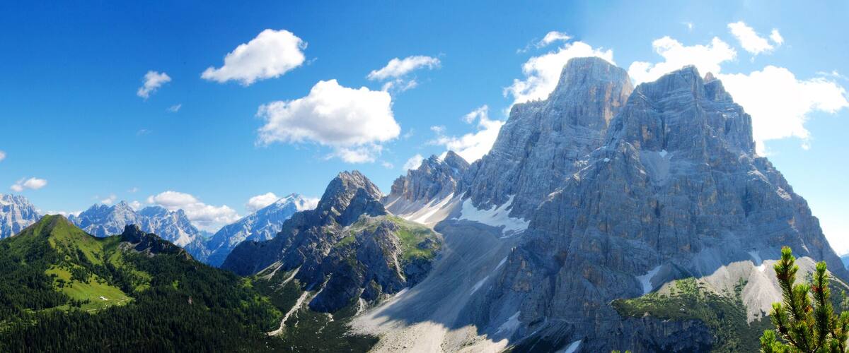 Ein Gebirge mit markanten Gipfeln, üppig grünen Tälern und blauem Himmel.