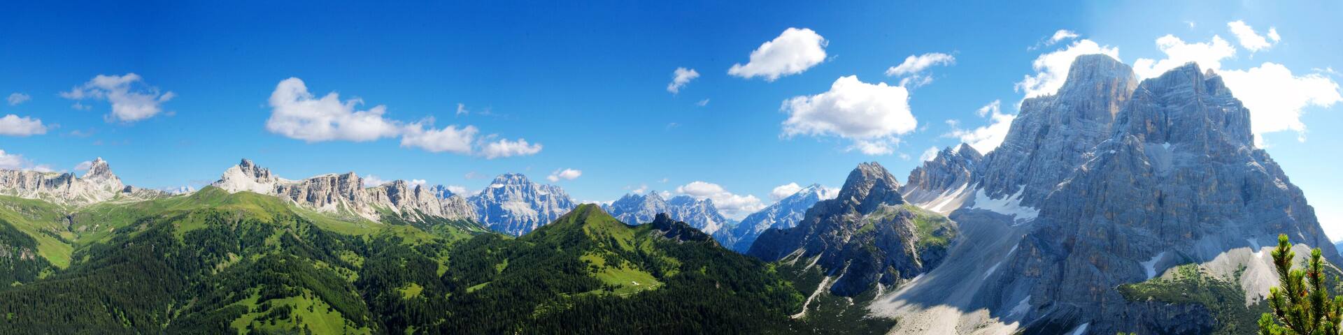 A mountain range with prominent peaks, lush green valleys, and a clear blue sky.