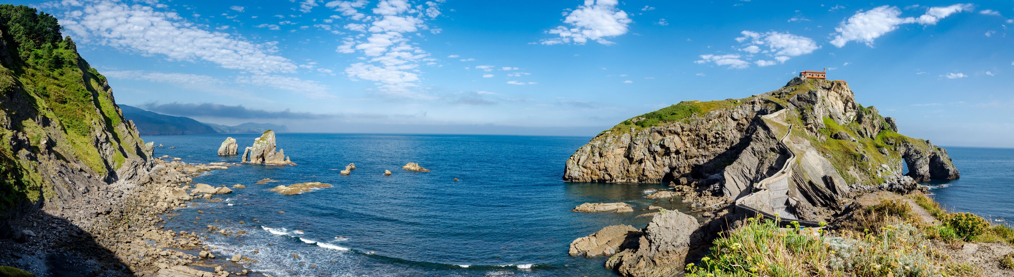 A coastal landscape with rocky cliffs, a lighthouse on a hill, and scattered boulders in the water.
