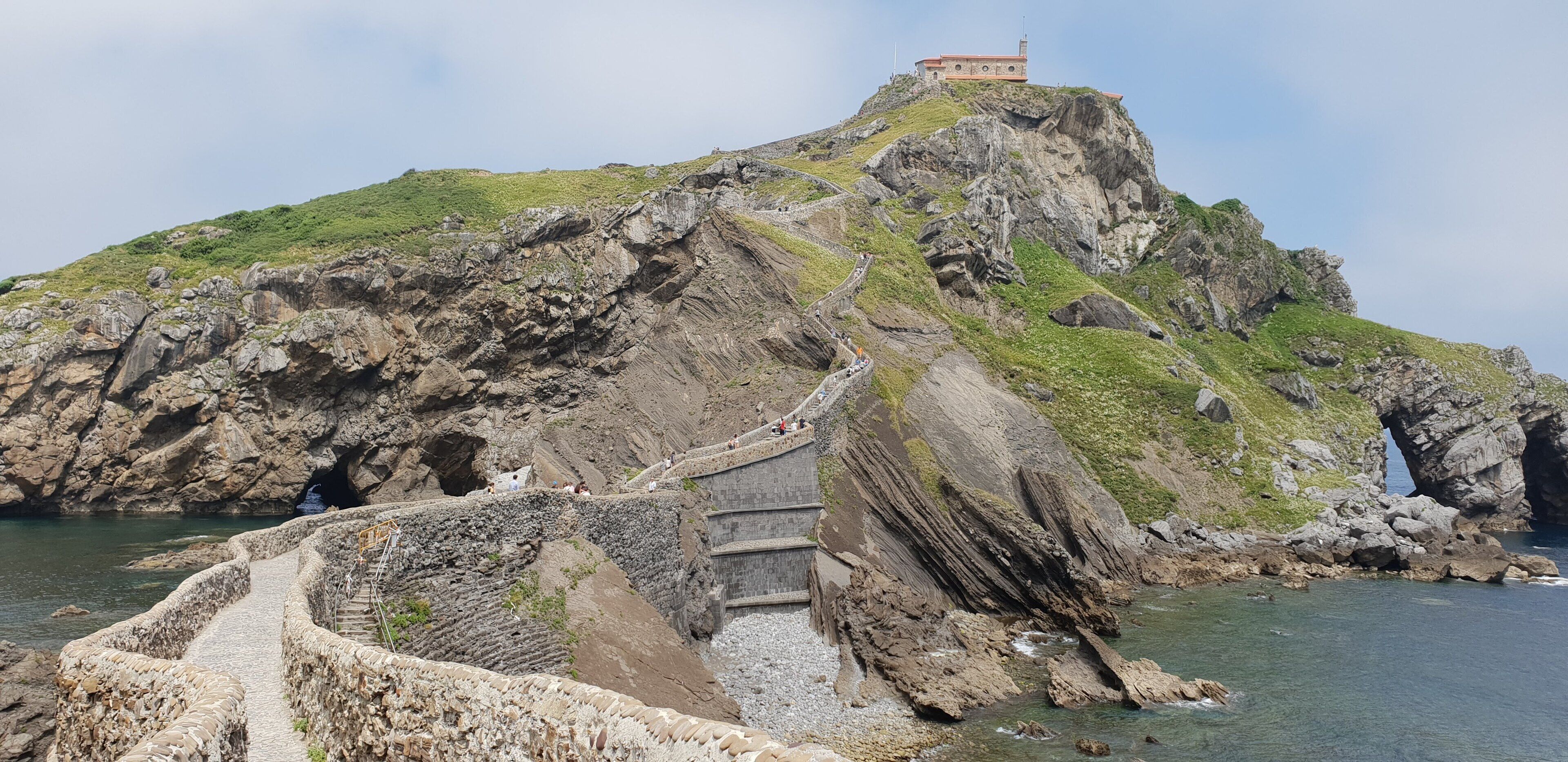 A rugged coastline with a winding stone pathway leading to a building on a hilltop.