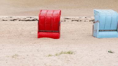 Three beach chairs in blue, red, and light blue colors on a sandy beach.