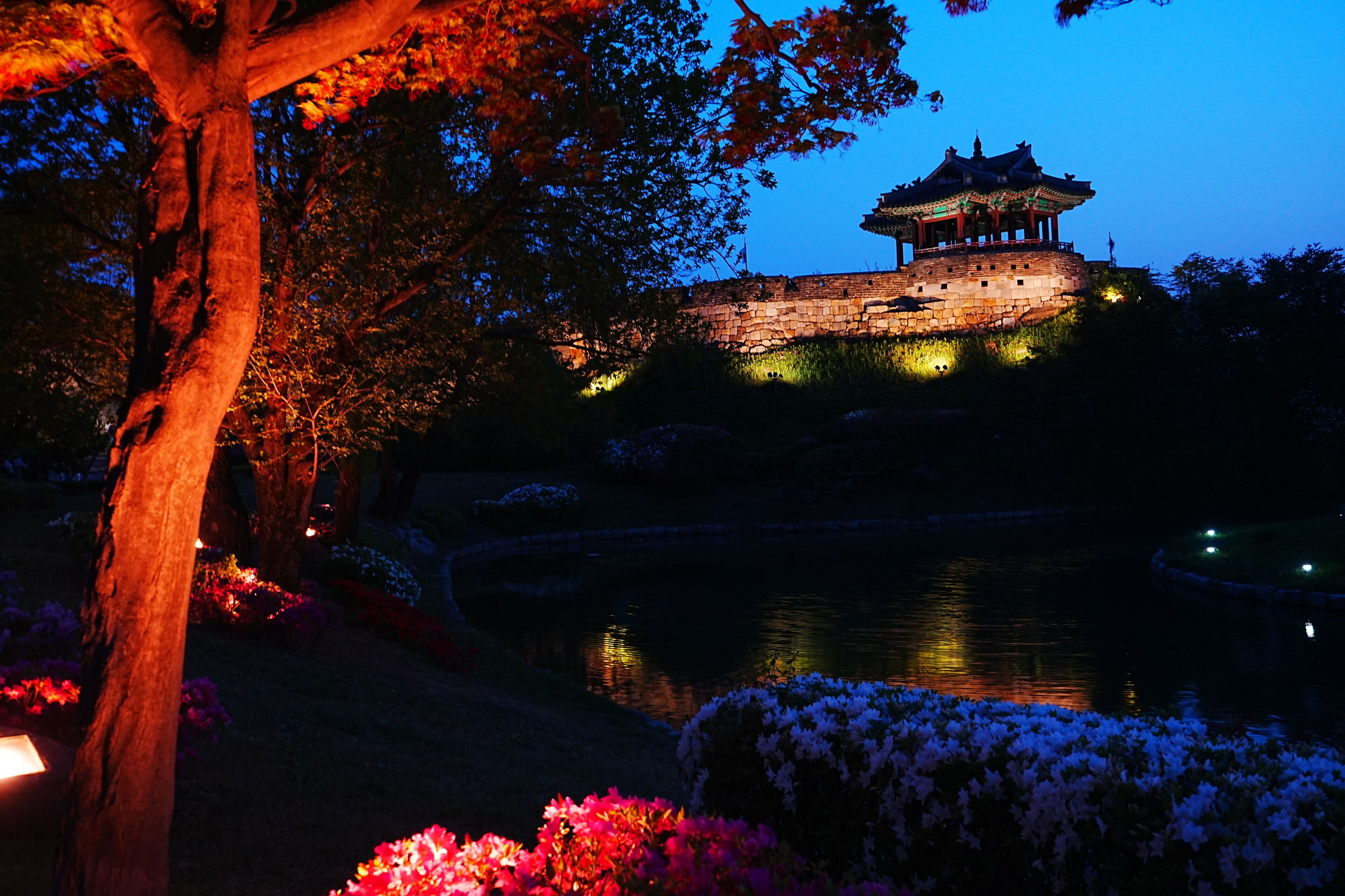 A traditional pagoda-style building with a stone base, surrounded by a body of water and illuminated by artificial lighting.