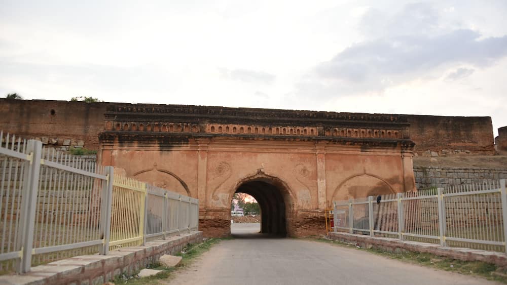 Un pont en pierre en arc surmontĂ© de garde-corps mĂ©talliques de part et dâautre, qui mĂšne Ă une porte.