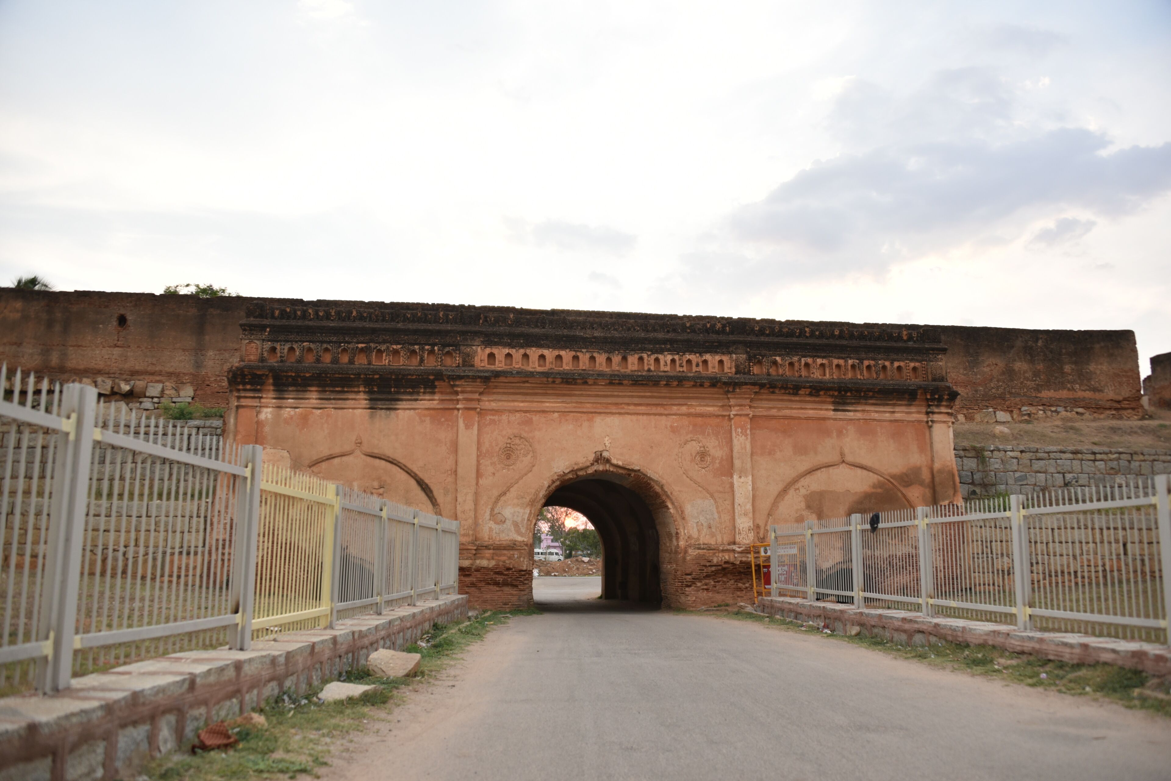 An arched stone bridge with metal railings on both sides, leading through a gate.