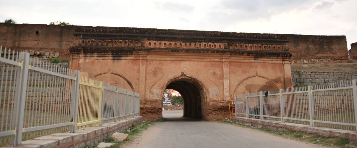 An arched stone bridge with metal railings on both sides, leading through a gate.