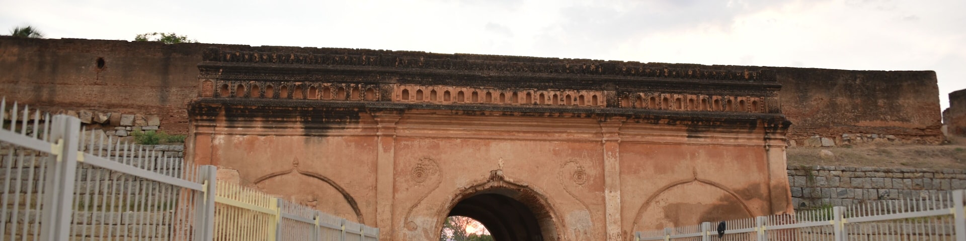 An arched stone bridge with metal railings on both sides, leading through a gate.