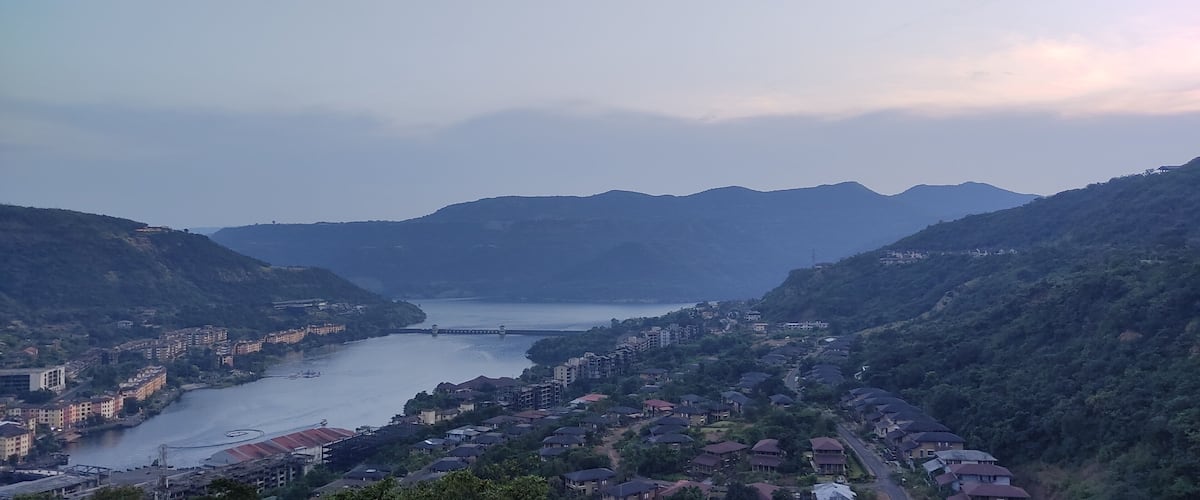 A river winding through a valley with residential buildings on both sides, surrounded by hills.