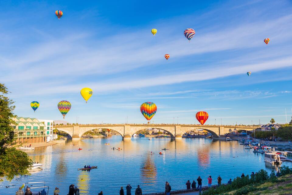 Un río con un puente, globos aerostáticos y barcos.