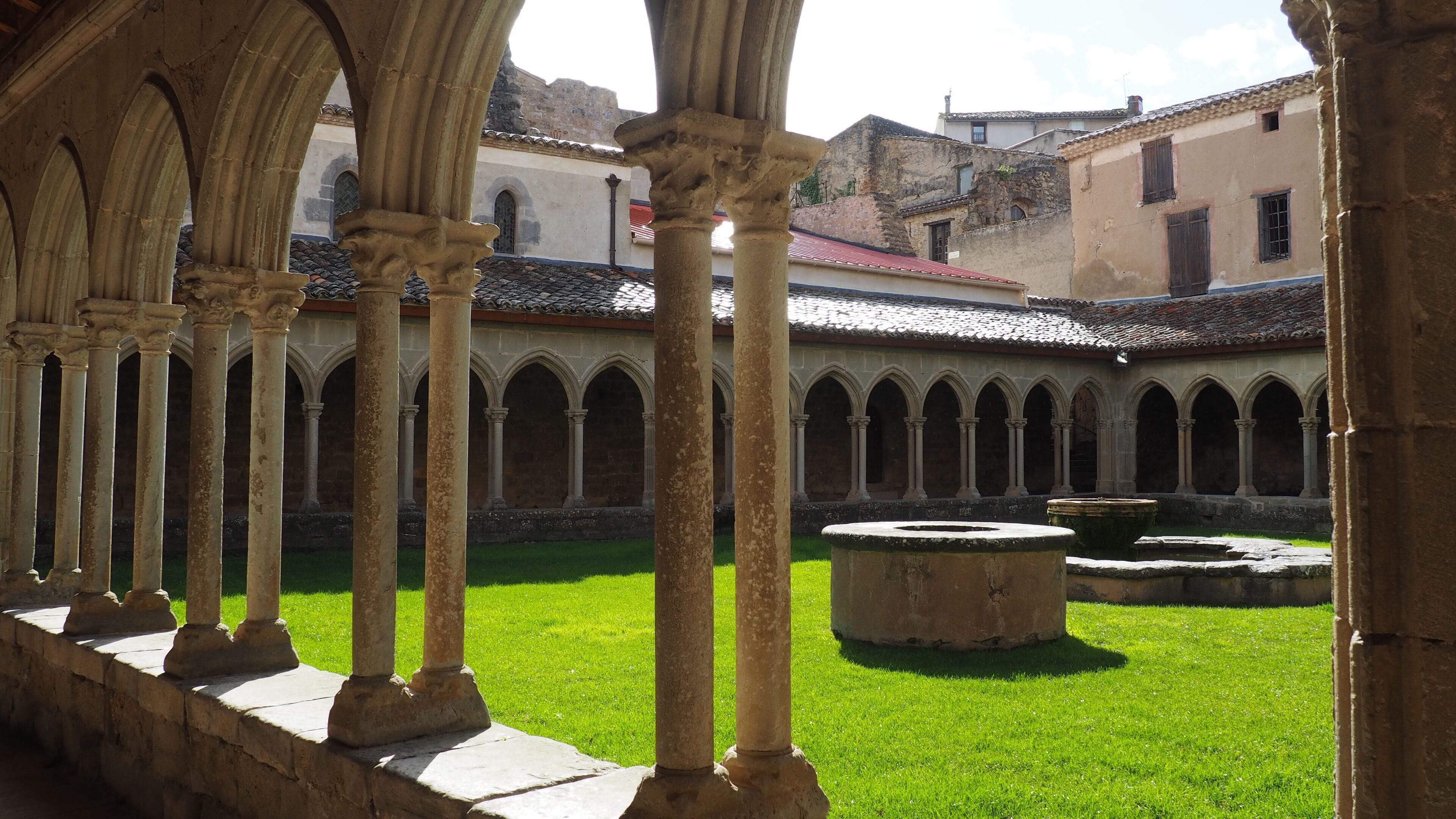 A courtyard with stone columns and arches, surrounded by buildings with tiled roofs.