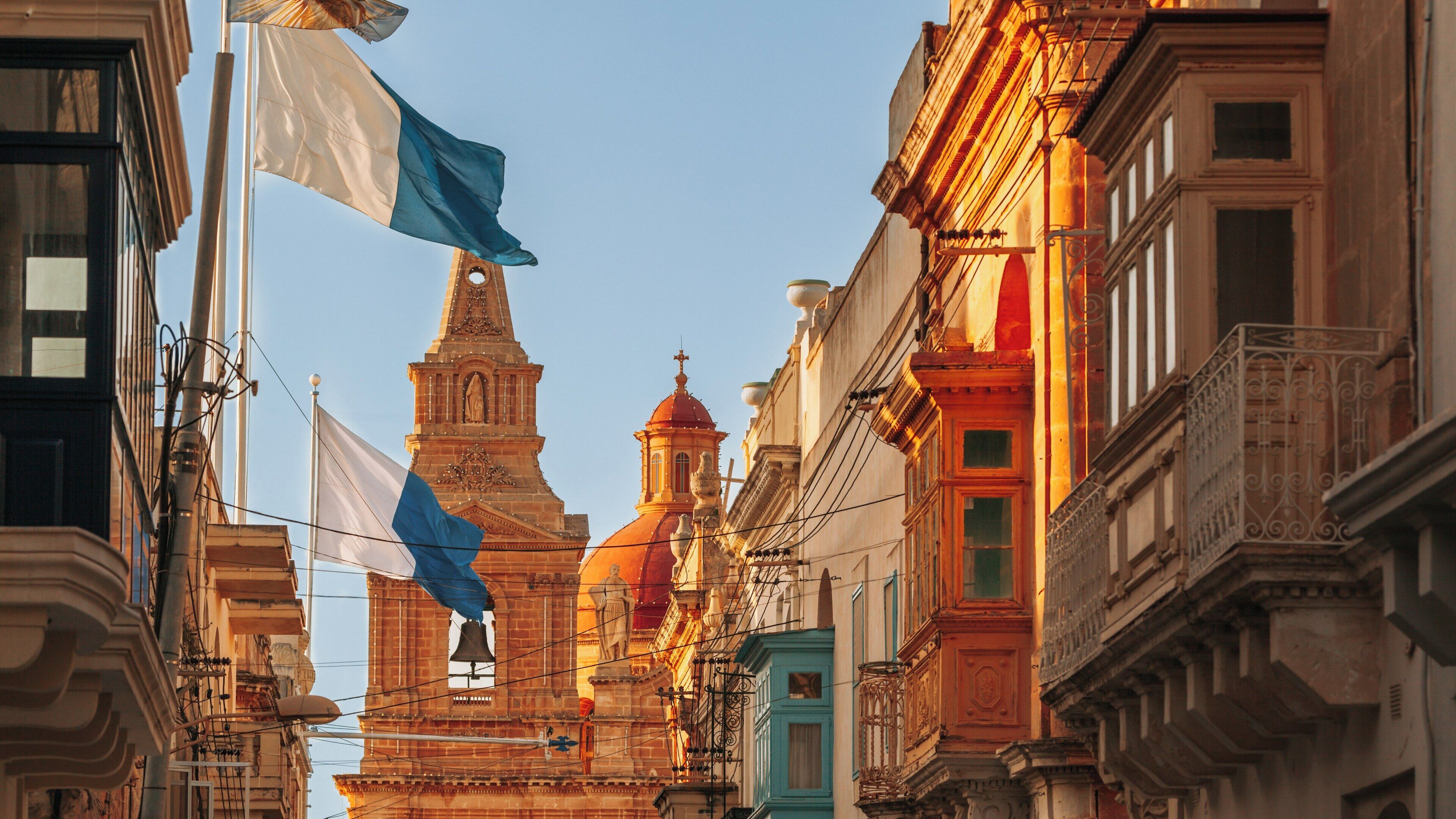 Mellieha Church towers above narrow streets adorned with colorful flags in Mellieha, Northern Region of Malta during late afternoon