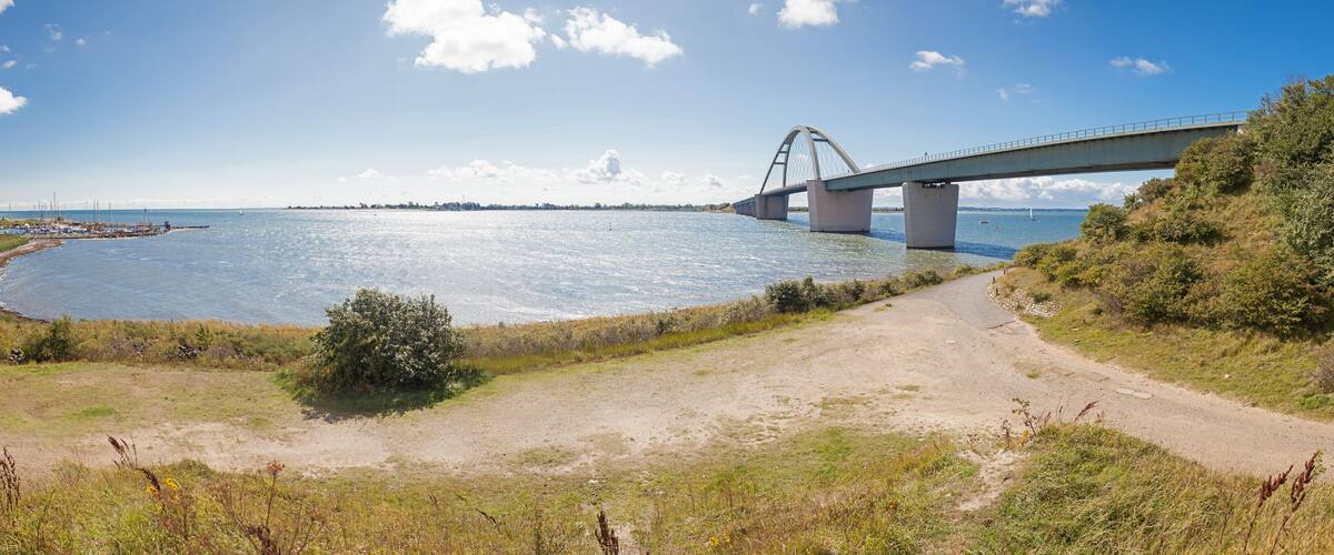 A coastal landscape with a bridge over water, a dirt path, and sparse vegetation.