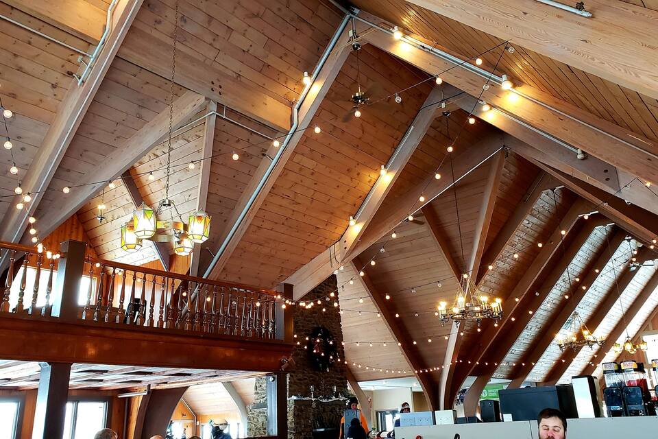 A wooden interior with high ceilings, exposed beams, and string lights.
