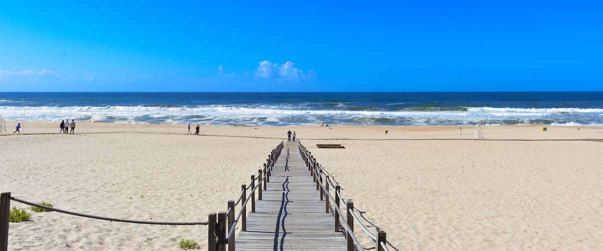 A beach with a wooden boardwalk leading to the ocean, sandy shore, and waves.
