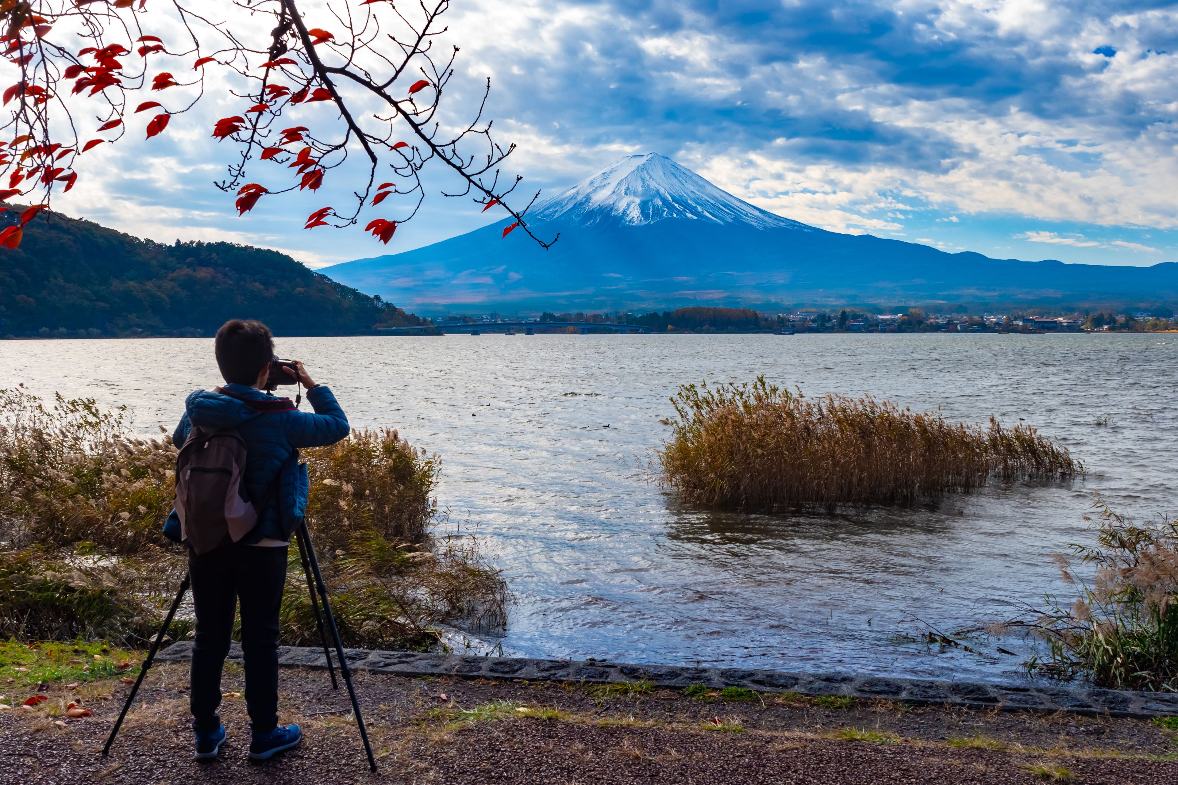 Une personne prend une photo d'une montagne, avec un lac au premier plan.