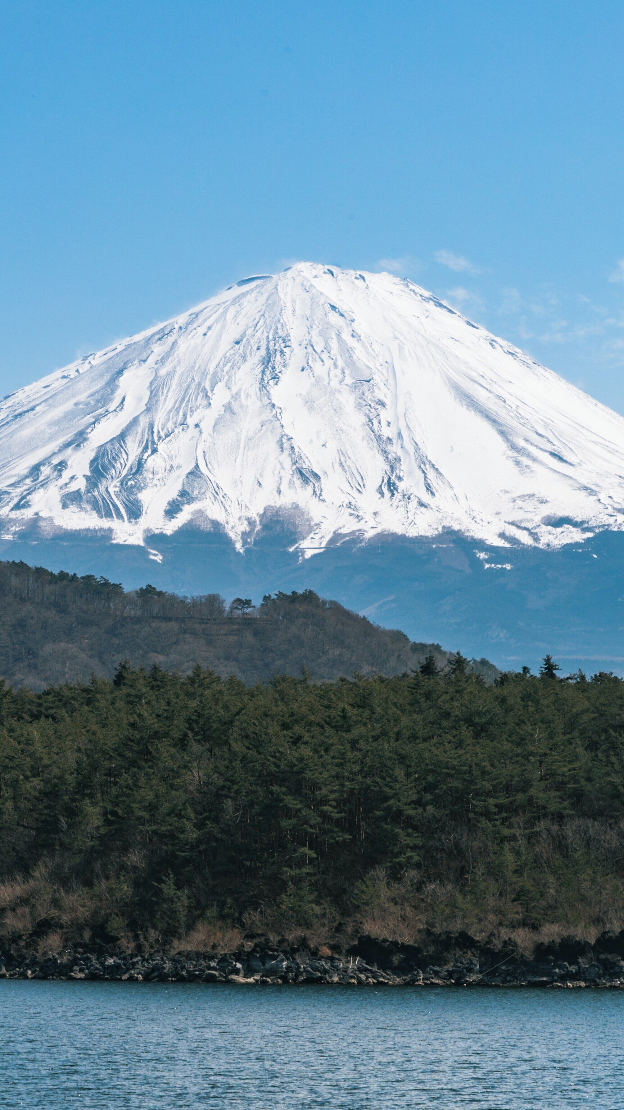 Snow-capped Mount Fuji towering over Lake Saiko in Kofu, Yamanashi Prefecture, Japan during clear blue skies