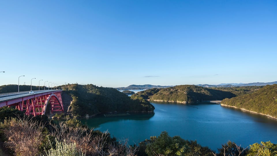 A red bridge over a calm river surrounded by hills.