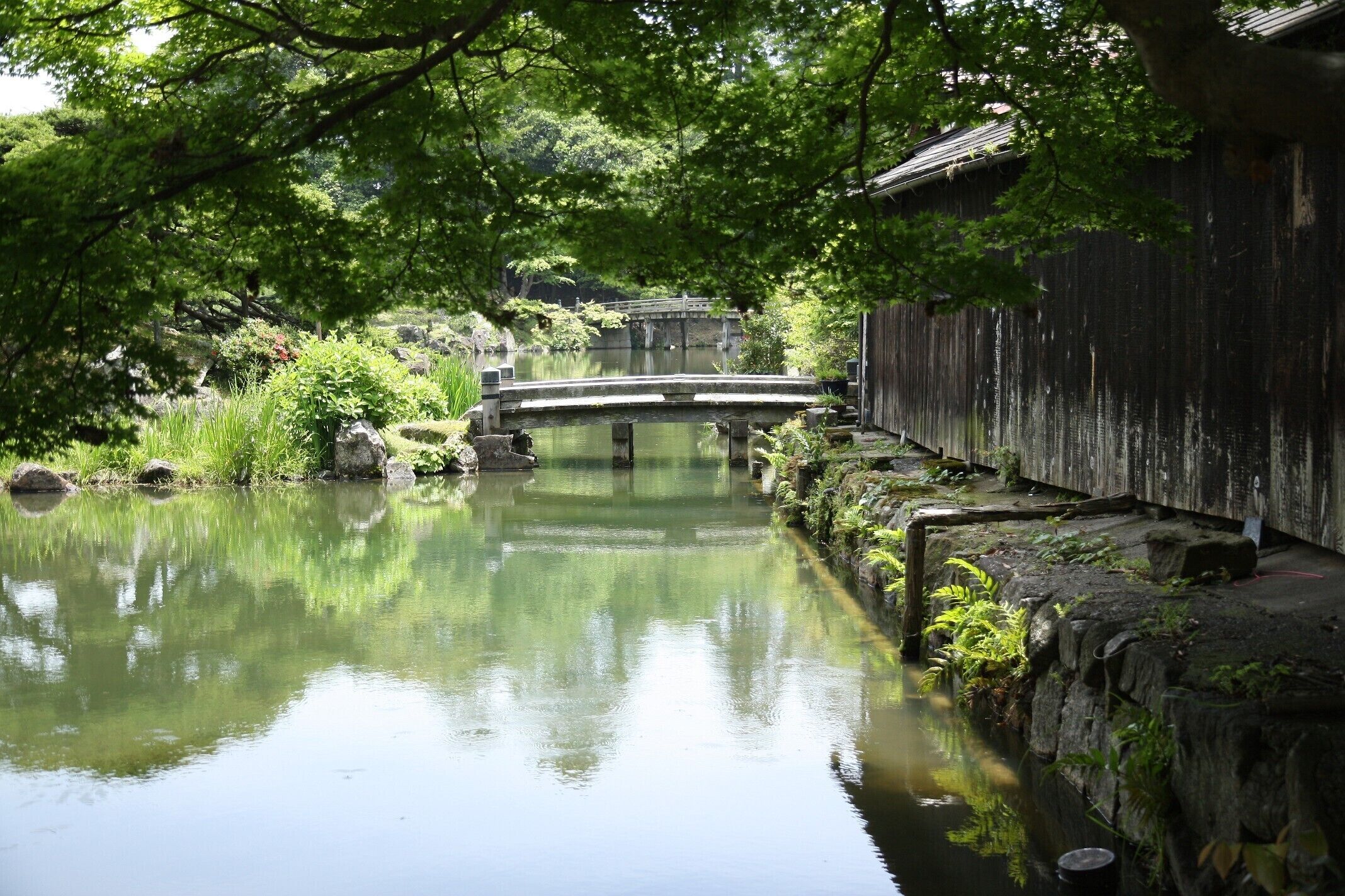 A tranquil river with a wooden bridge and a traditional building.
