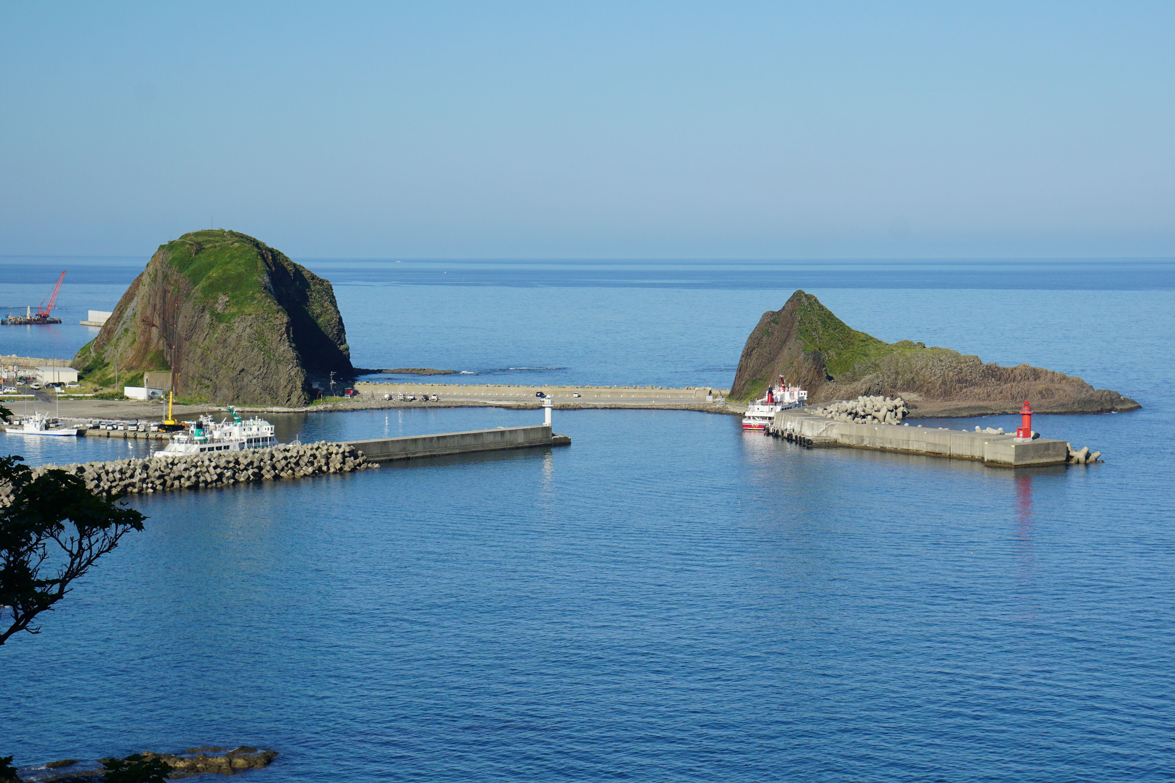 A coastal scene with two prominent rocky islands, a pier, and a lighthouse.