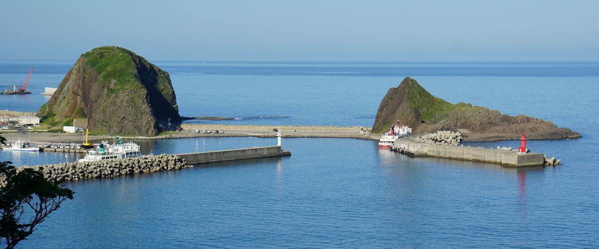 A coastal scene with two prominent rocky islands, a pier, and a lighthouse.