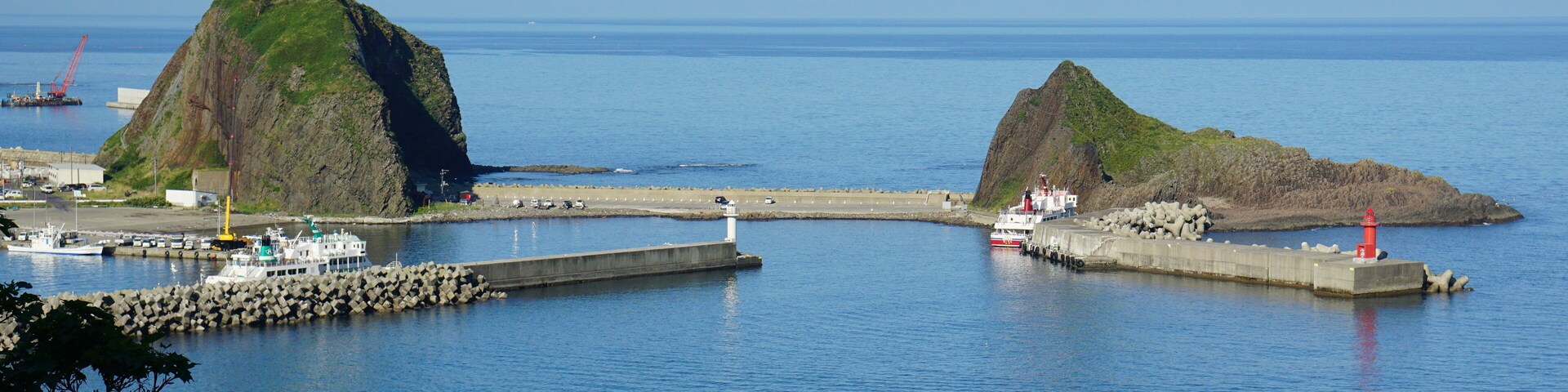 A coastal scene with two prominent rocky islands, a pier, and a lighthouse.