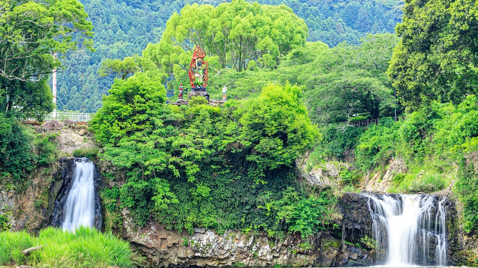 A waterfall surrounded by lush greenery and a statue.